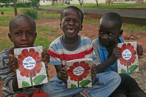 Three boys show off the BFA books they were given as a reward for helping set up a community library in The Gambia.